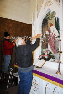 MIKE LIETZOW (left) and Neil Altman put some icicle Christmas lights across the front of the altar. (Photo by Peter Jakey)