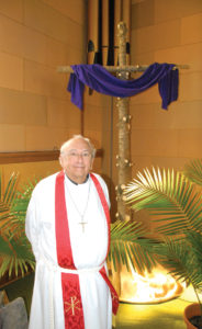 READY FOR Easter in Belknap! The Rev. Keith Schneider will be leading Easter services Sunday at St. Michael Lutheran Church. He stands next to a cross that’s made from wood that was the trunk of the Christmas tree in December. (Photo by Peter Jakey)